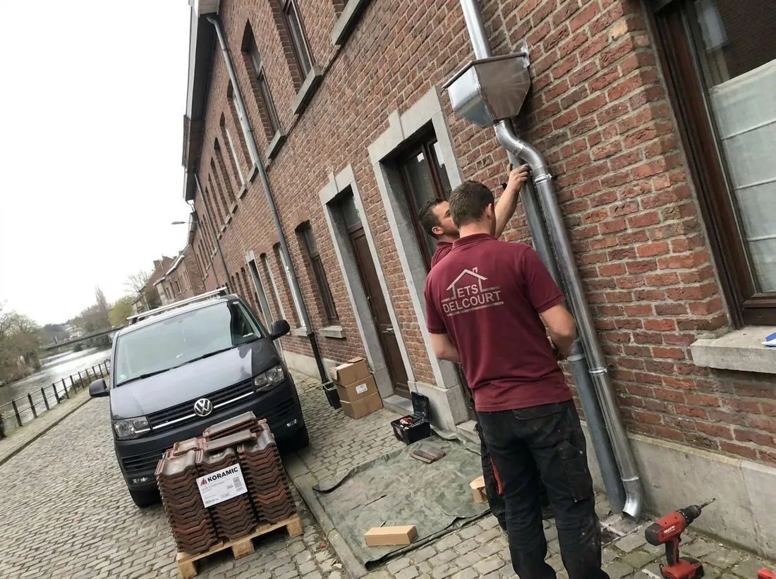 Artisan Ets Delcourt fixant une descente d'eau en zinc sur une façade en briques